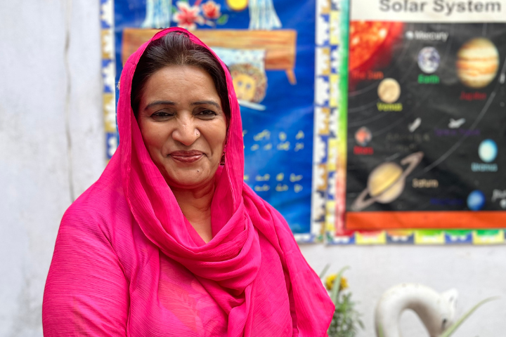 A woman in a bright pink shawl stands outside a classroom. 