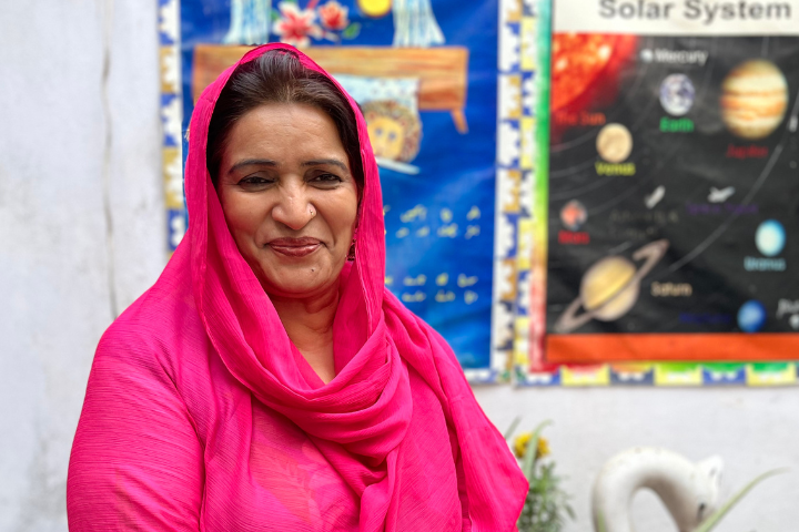 A woman in a bright pink shawl stands outside a classroom.