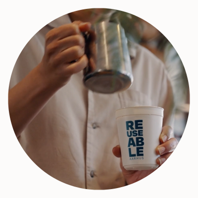 A barista pours milk into a reusable cup.