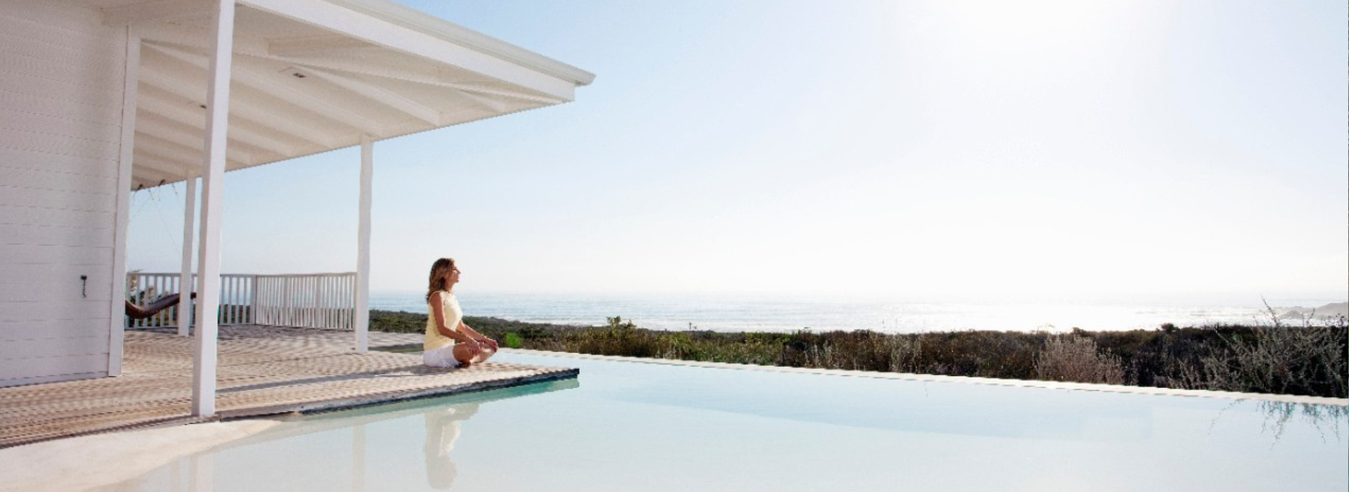 A woman sits at the edge of a pool overlooking a valley.