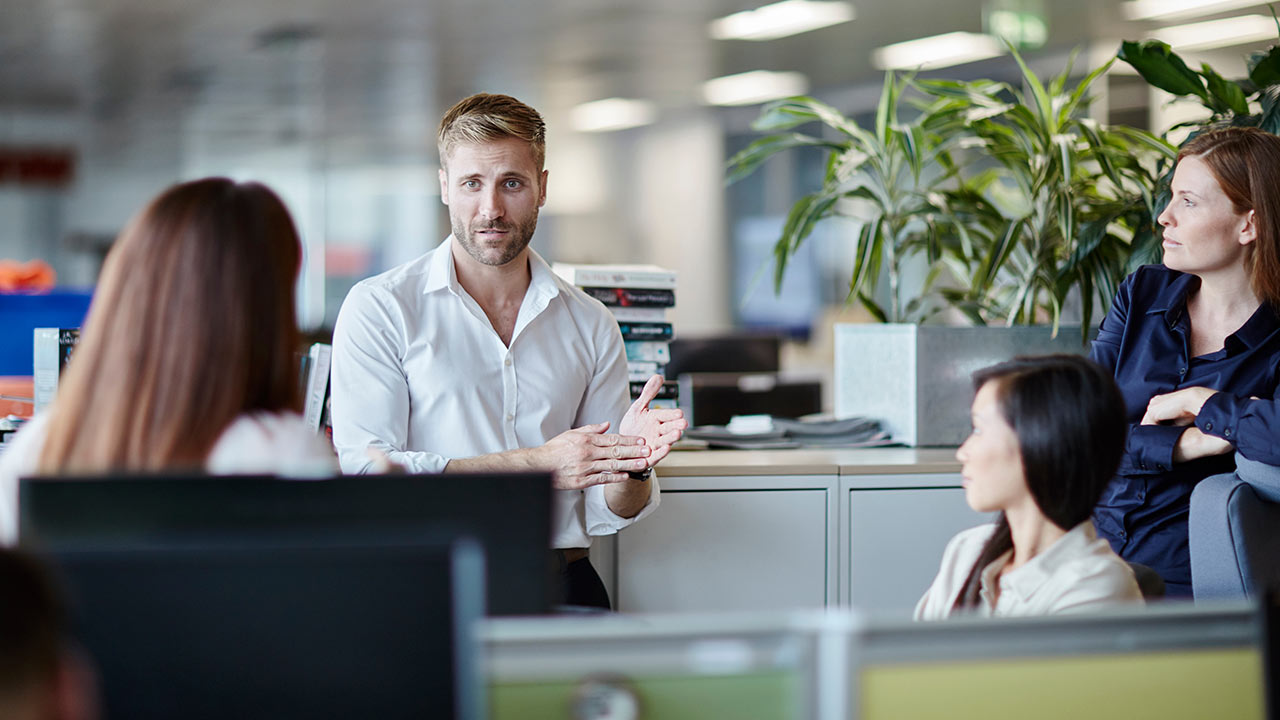 A man talks to his colleagues in an office. 