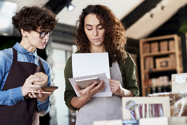 A worker looks at paperwork while another holds a writing implement and looks on. 