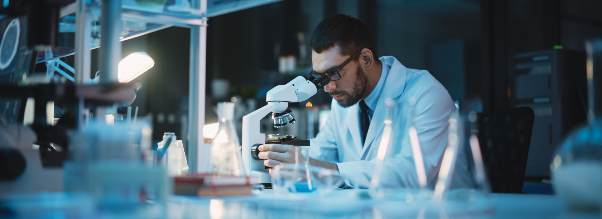 Photo of a man in a lab coat looking through a microscope