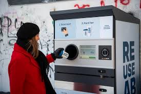 A woman deposits a recyclable cup in a Tomra reverse vending machine. 