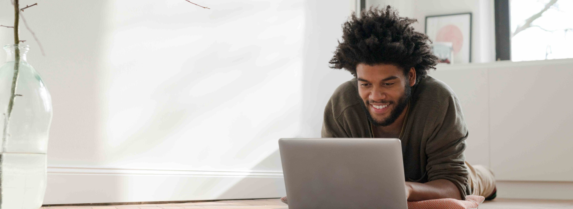 A man laying on the floor and smiling at his laptop.