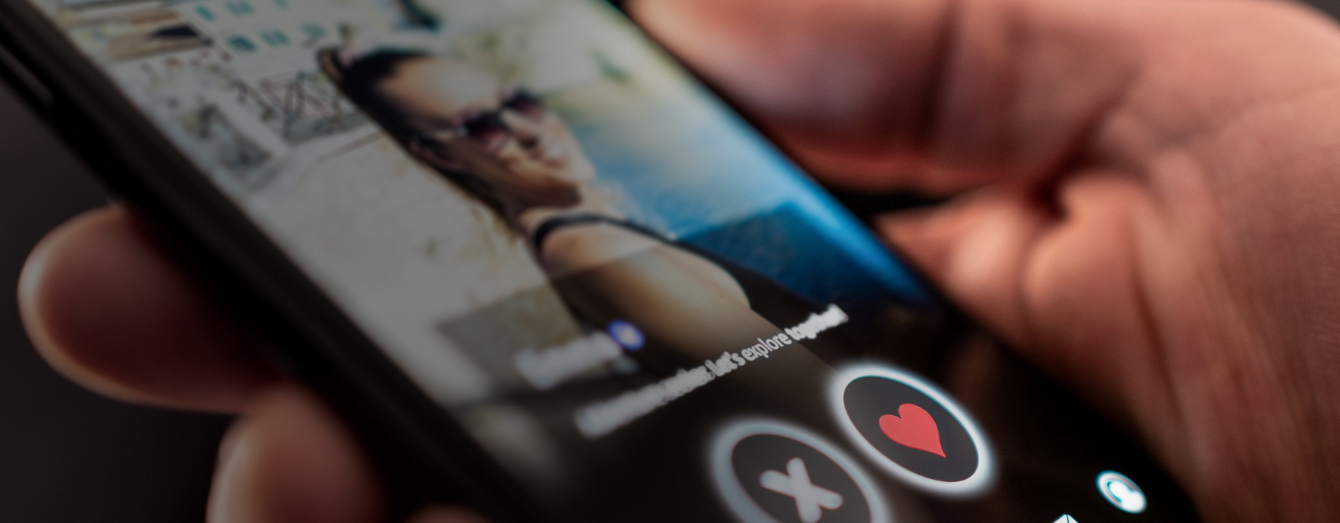 A person holds a smartphone with a dating app open showing a woman and a button with a heart on it. 