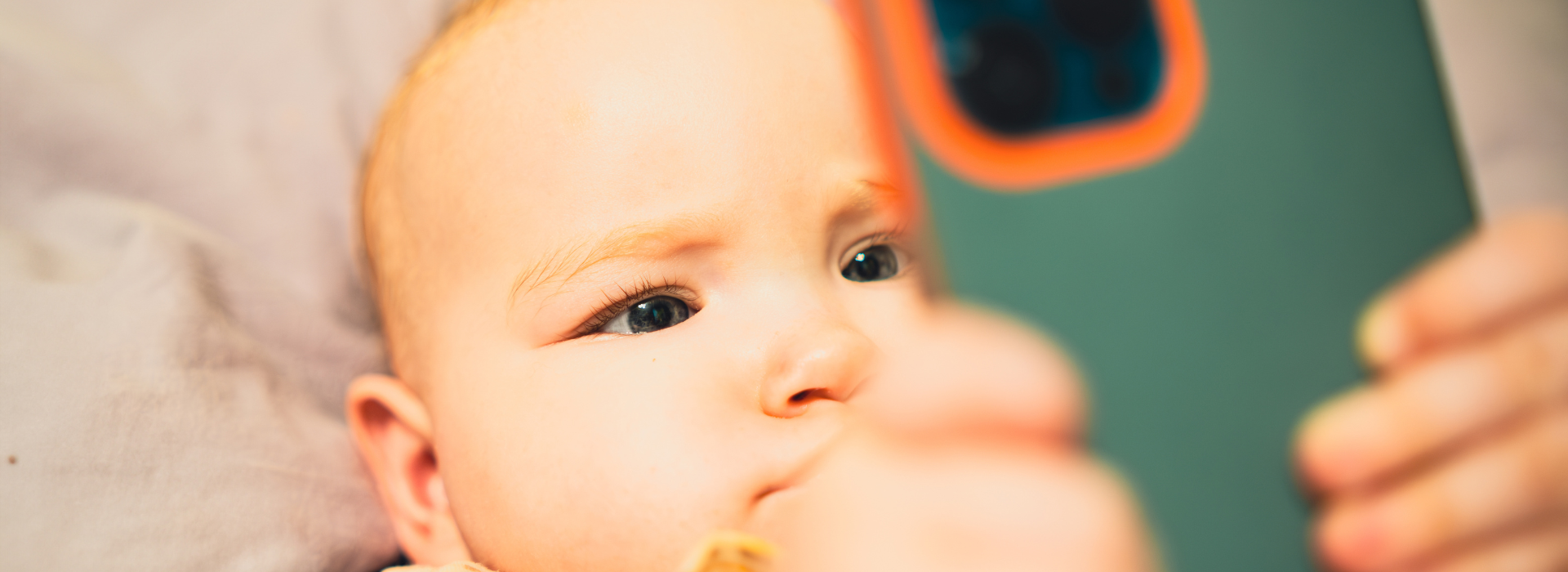 A baby on its back looks at a smartphone. 