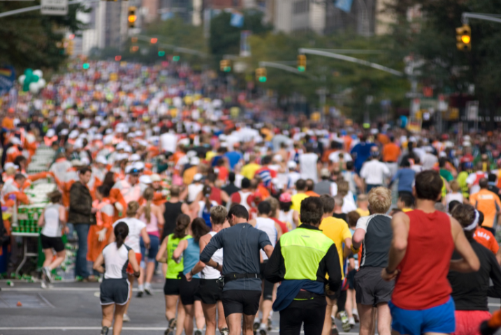 A stream of runners in colorful running gear run down a street in New York City during the NYC Marathon.