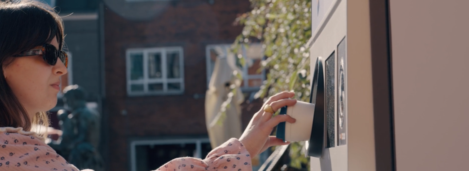 A woman returns a reusable cup to a reverse vending machine to receive her deposit back. 