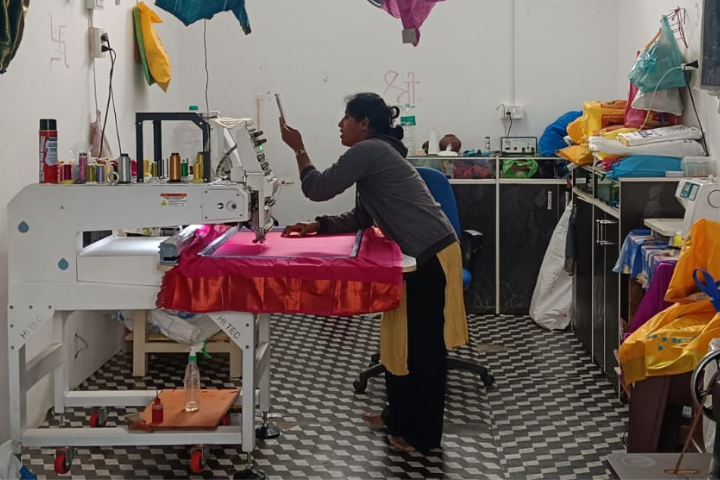 Sweta YM stands over a swath of pink fabric in her embroidery shop. 