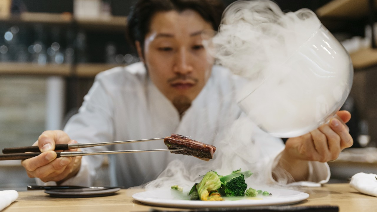 A chef puts a piece of meat on a plate cloaked in smoke.
